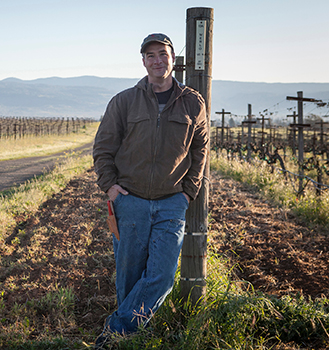 Mike Hendry, in a hat and jacket, in the vineyard.